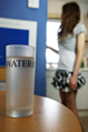 A glass of water on a table with a girl in a miniskirt in the background
