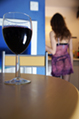 A glass of red wine on a table with a girl in a sheer slip and lingerie in the background