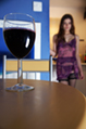 A glass of red wine on a table with a girl in a sheer slip and lingerie in the background