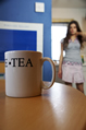 A mug of tea on a table with a girl in a short skirt in the background