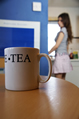 A mug of tea on a table with a girl in a short skirt in the background