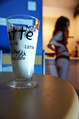 A glass of milk on a table with a girl in a vest top and knickers in the background
