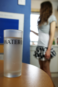 A glass of water on a table with a girl in a miniskirt in the background
