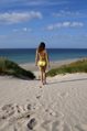 woman in yellow bikini walks through sand dunes towards beach and sea