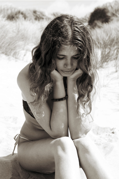 Girl in tie-side bikini sits thinking in the sand dunes