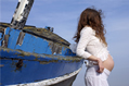 pregnant female in white lace rests against a blue boat