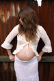pregnant woman in white lace leans against rusted iron