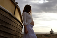 woman in white lace leans on fishing boat with second boat on the horizon