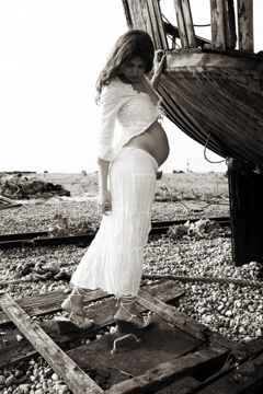 pregnant girl in white lace leans against an old boat