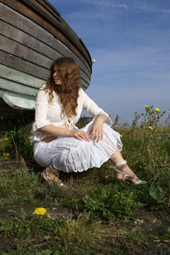 female in white lace sitting by a boat and looking away to far off