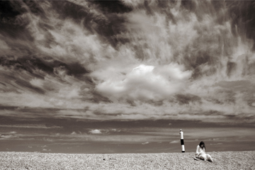 Female and lighthouse on a shingle spit below dramatic sky