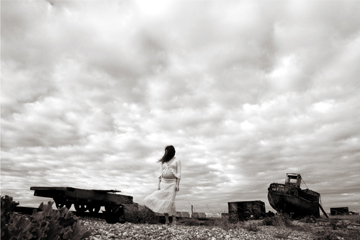 woman in white lace walks across a bleak landscape