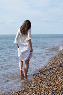 female in white lace paddles along the shore