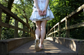 Girl in short denim skirt and sandals walks across a wooden bridge into the woods