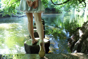 Girl in short denim skirt and sandals on stepping stones across a stream