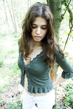 Alluring female with long brunette hair leans against a tree 